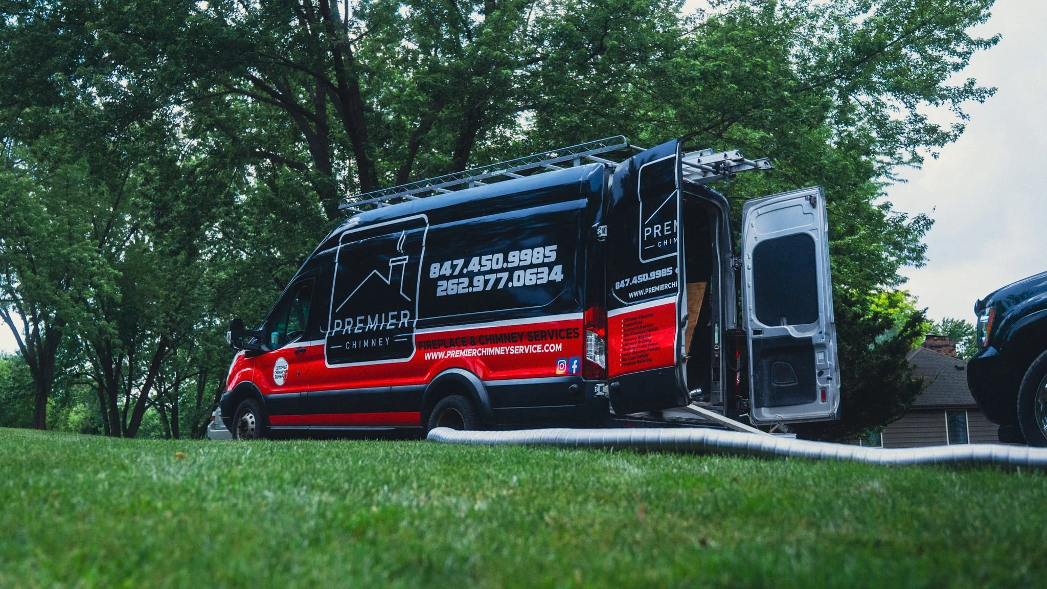 Service van with ladder and hoses on lawn for chimney sweep service