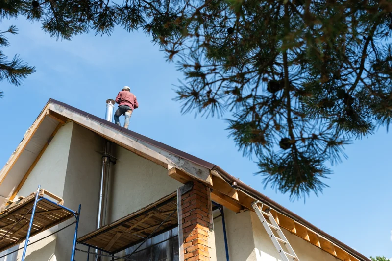 Roofer installing stainless steel chimney liner on a sloped roof beside scaffolding