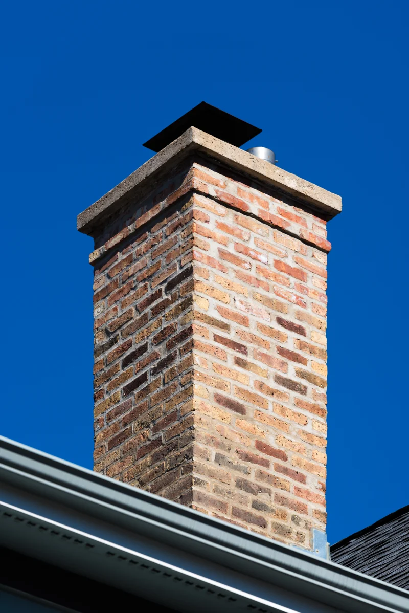 Brick chimney with metal chimney cap on rooftop against clear blue sky – Chimney caps