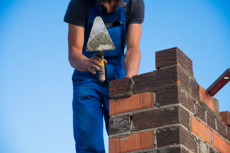 Worker applying mortar to brick chimney stack during masonry repair