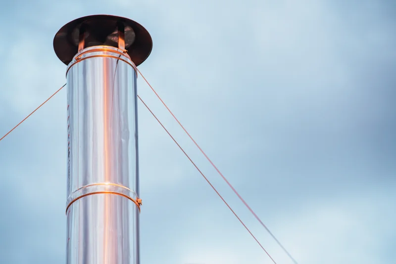 Shiny stainless steel chimney liner supported by guide cables against sky during Stainless steel chimney liners installation
