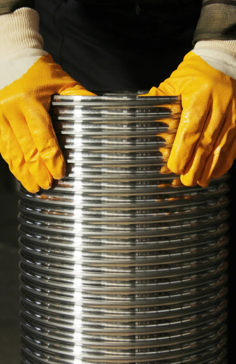 Section of corrugated stainless steel chimney liners held by yellow-gloved hands